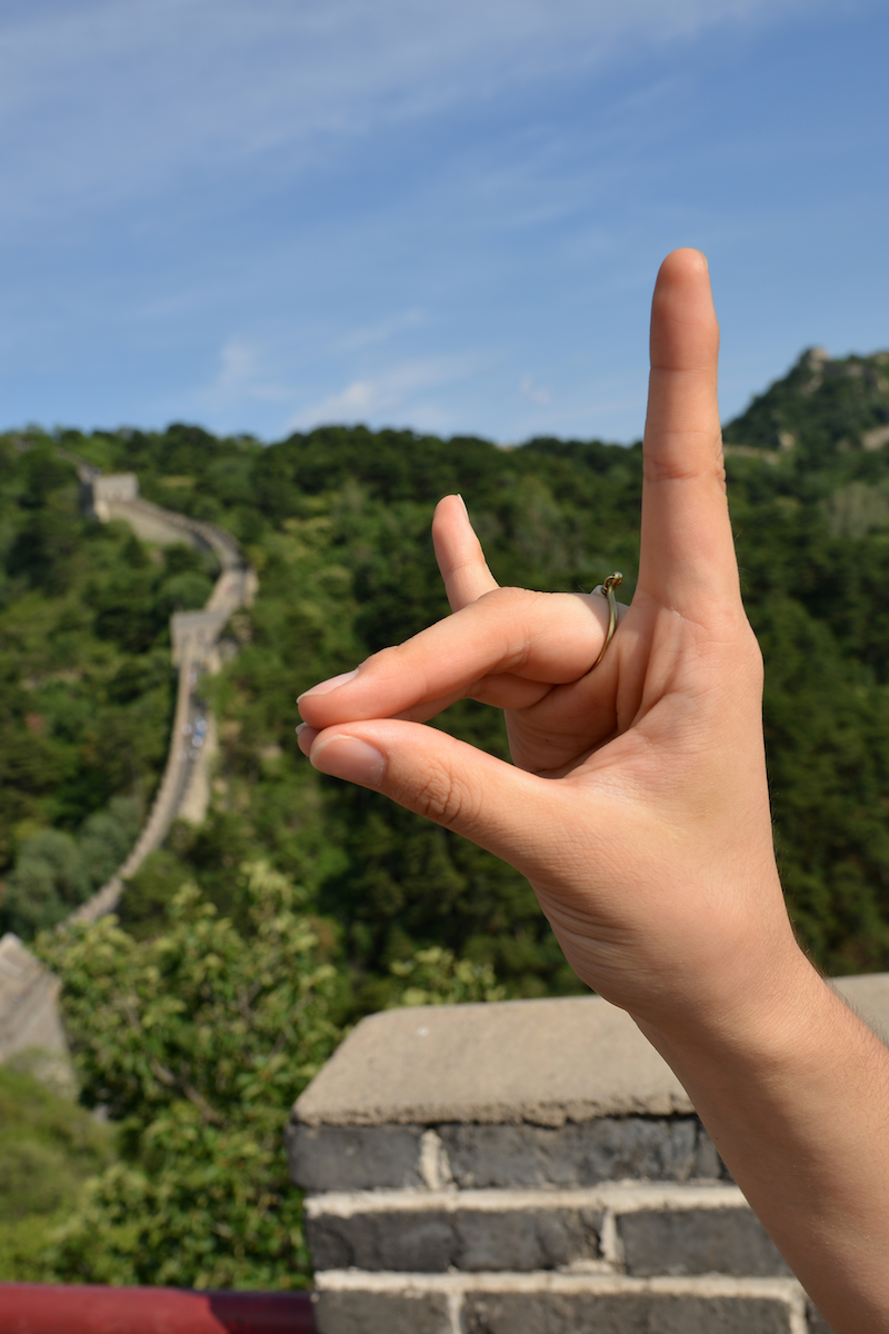 A hand making the NC State Wolfpack hand gesture at the Great Wall of China.
