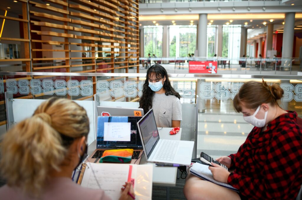 Three students with masks on studying at their computers around a table in Talley Student Union.